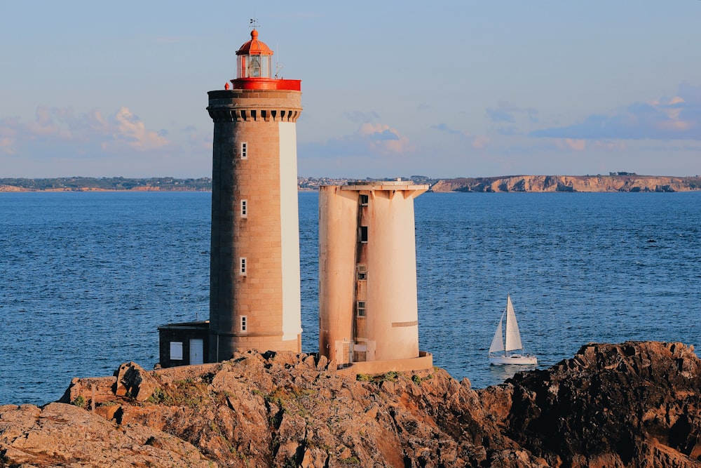 Faro marrón y blanco a través de un velero blanco