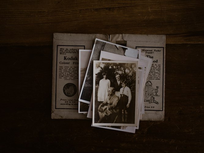A stack of old faded photographs and a magnifying glass resting on a wooden table