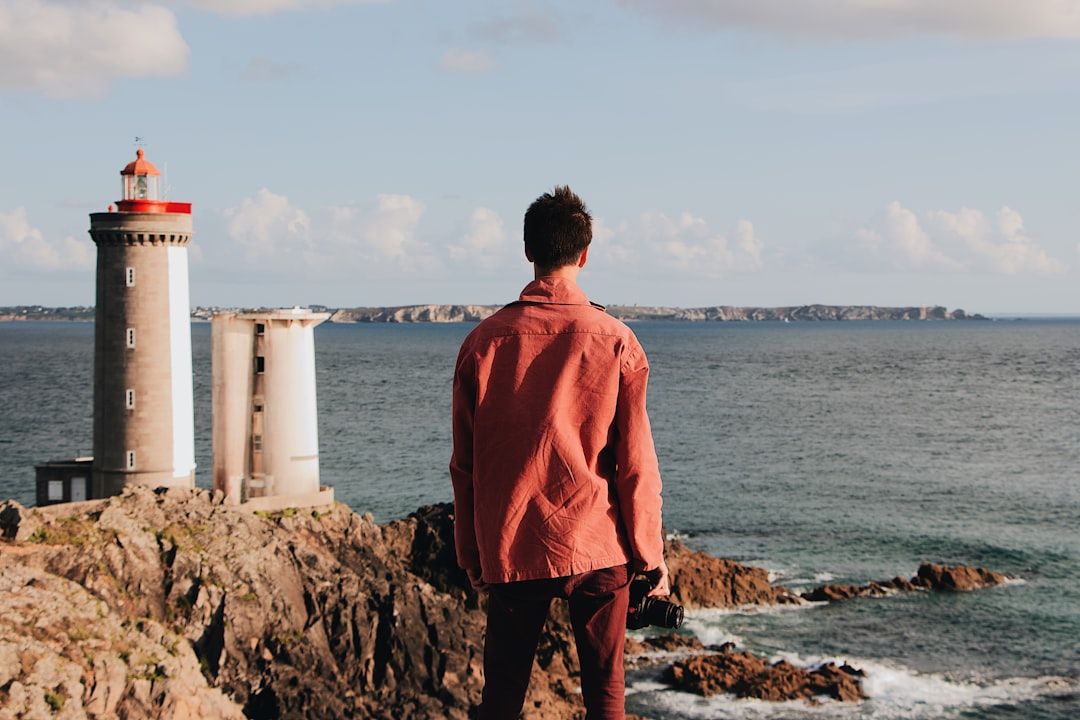 man standing on brown rocks near brown and white lighthouse