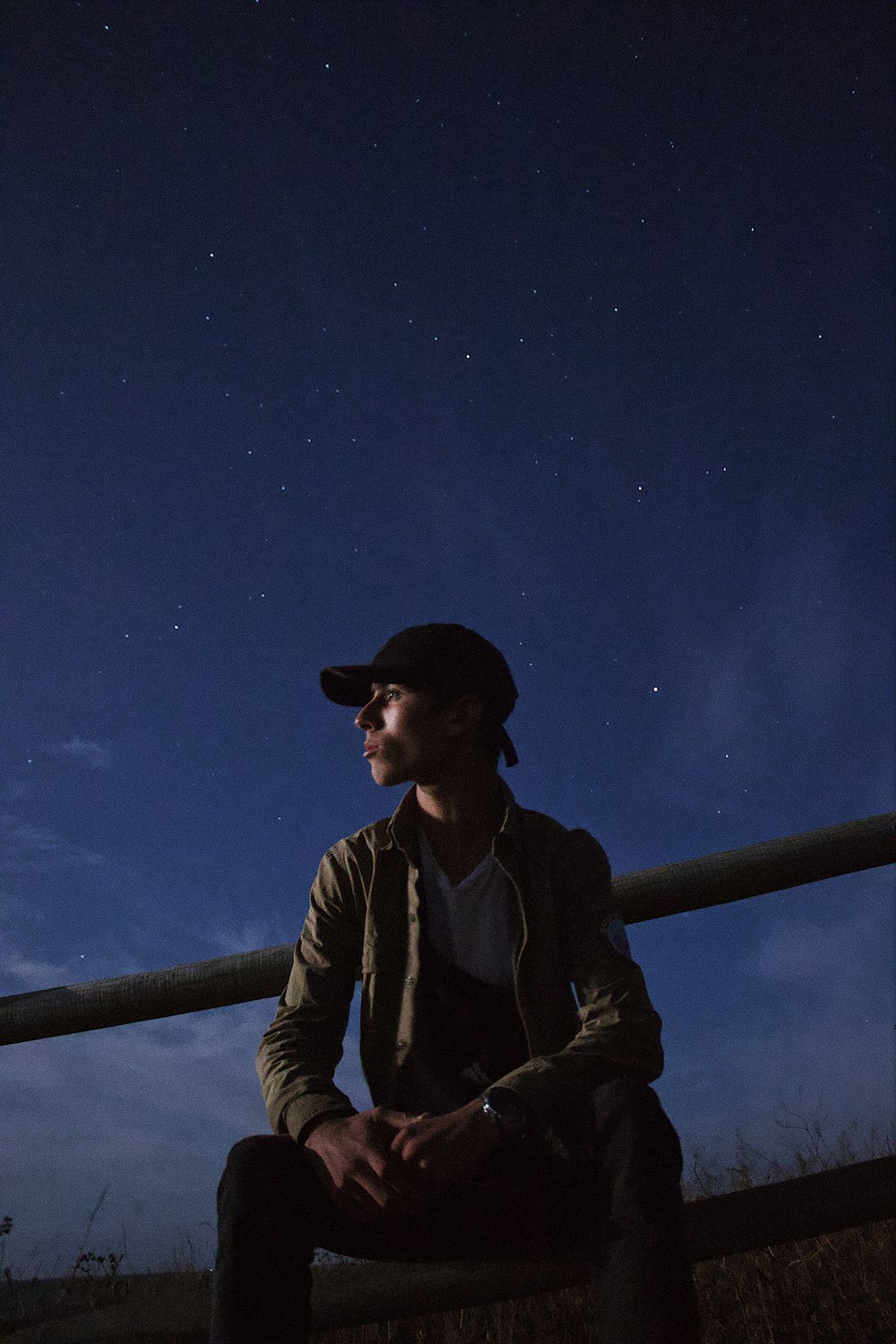 man sitting on railing during nighttime