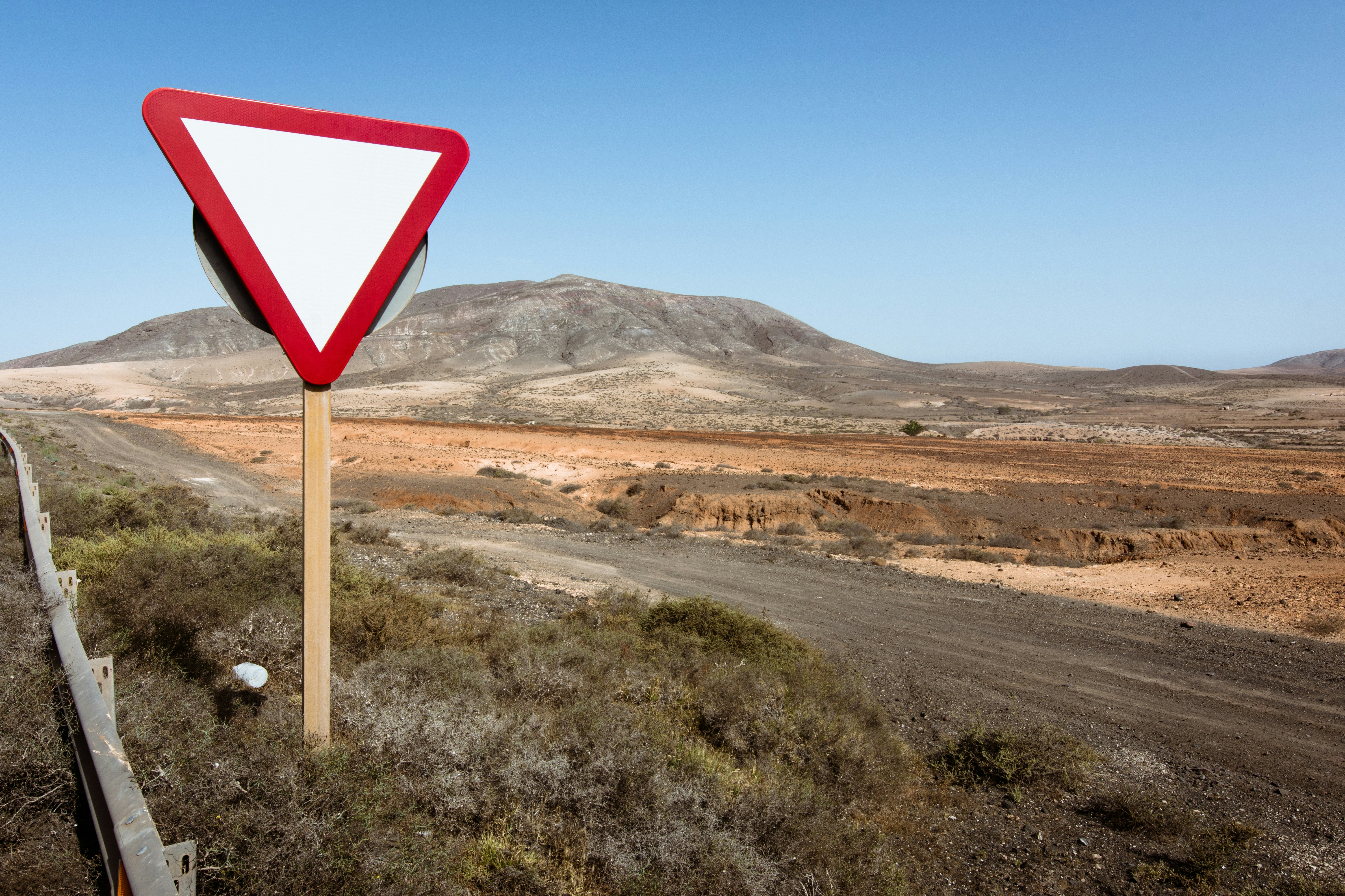 A blank yield sign stands beside a rural desert road with mountains in the background.