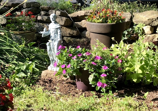 A serene garden scene featuring a detailed concrete statue of a playful cherub nestled among blooming flowers.