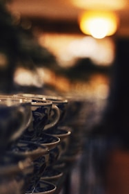 A row of ornately decorated ceramic cups is stacked neatly, creating a visually pleasing and symmetrical line. The image has a soft focus effect, with the background blurred and a warm light glowing in the upper right corner. The overall aesthetic conveys a sense of calm and order.