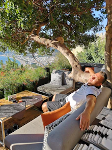 A comfortable outdoor loveseat set under a leafy tree with soft cushions and a small table.