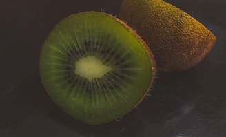 A close-up shot of a vibrant kiwi fruit sliced open, highlighting its bright green flesh and tiny black seeds.