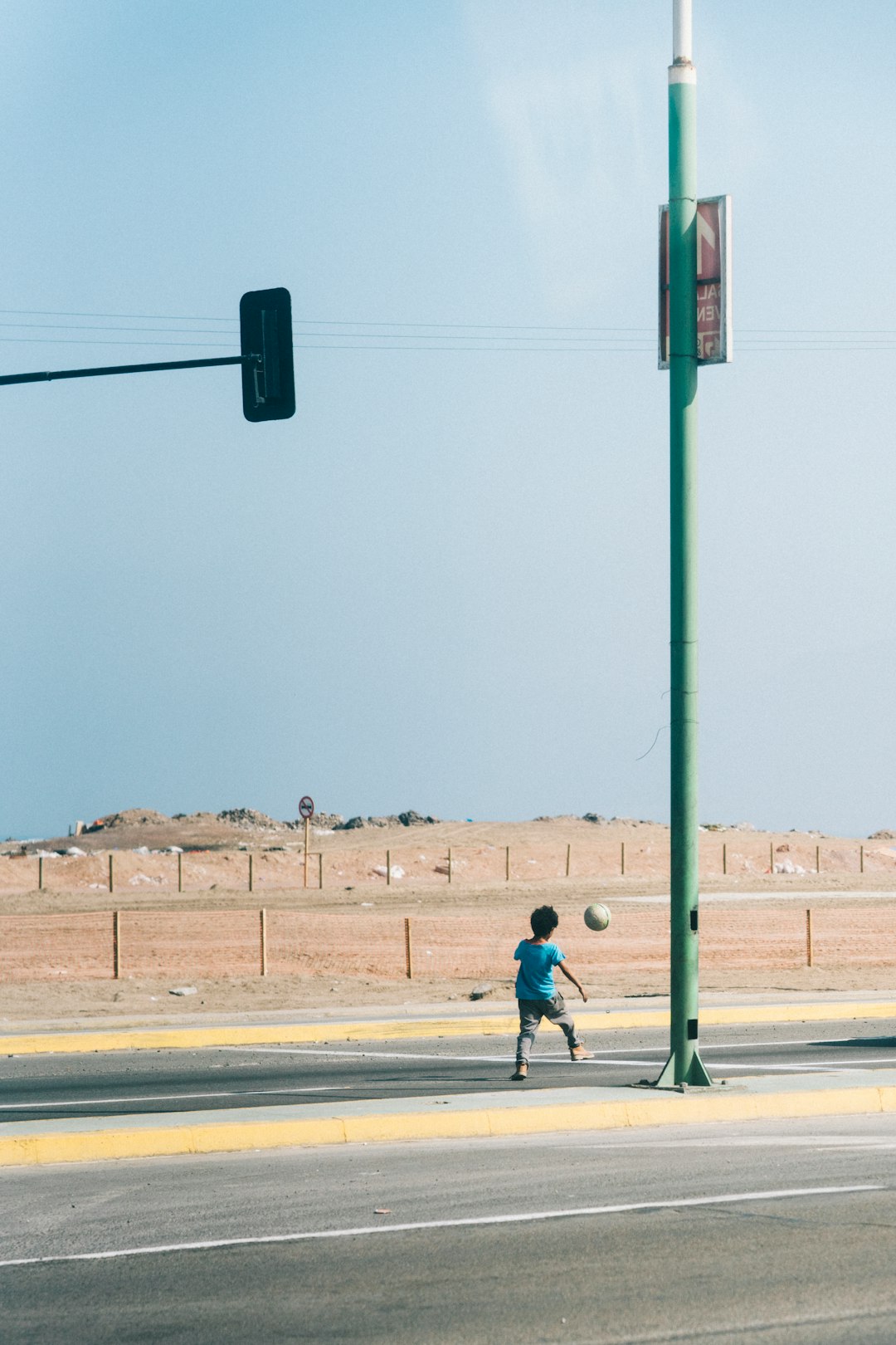 boy wearing blue shirt playing soccer on street