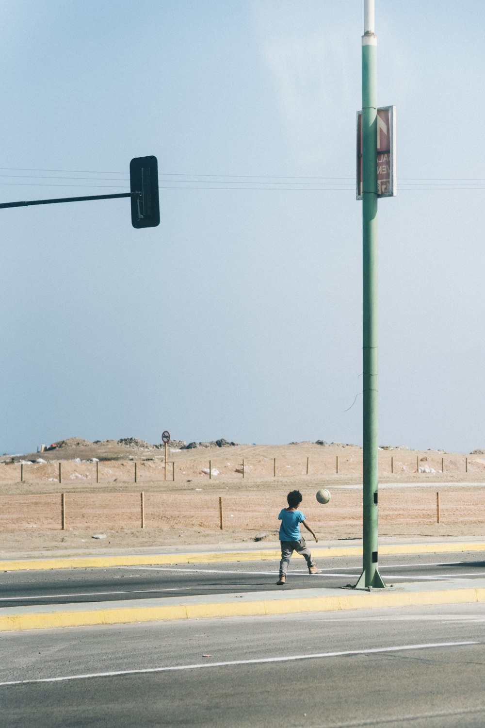 boy wearing blue shirt playing soccer on street