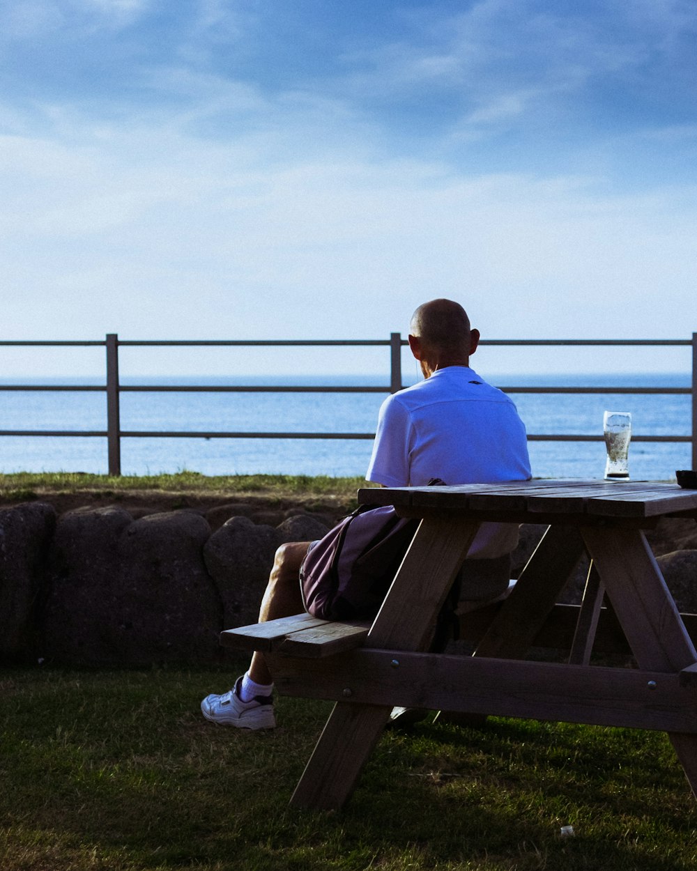 man sitting near table and facing on blue sea under blue and white skies