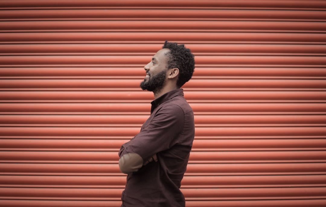 man in brown dress shirt standing near orange roller shutter