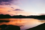 A serene sunset over a quiet lake with vibrant orange and pink hues reflecting on the water.