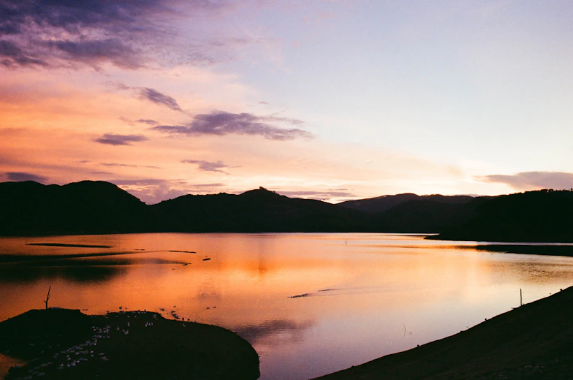 A serene sunset over a calm lake reflecting vibrant orange and purple hues.