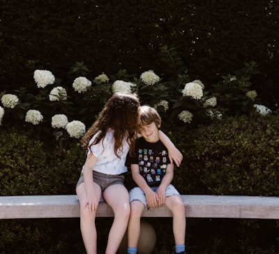 two toddler girl and boy sitting on concrete bench near outdoor during daytime
