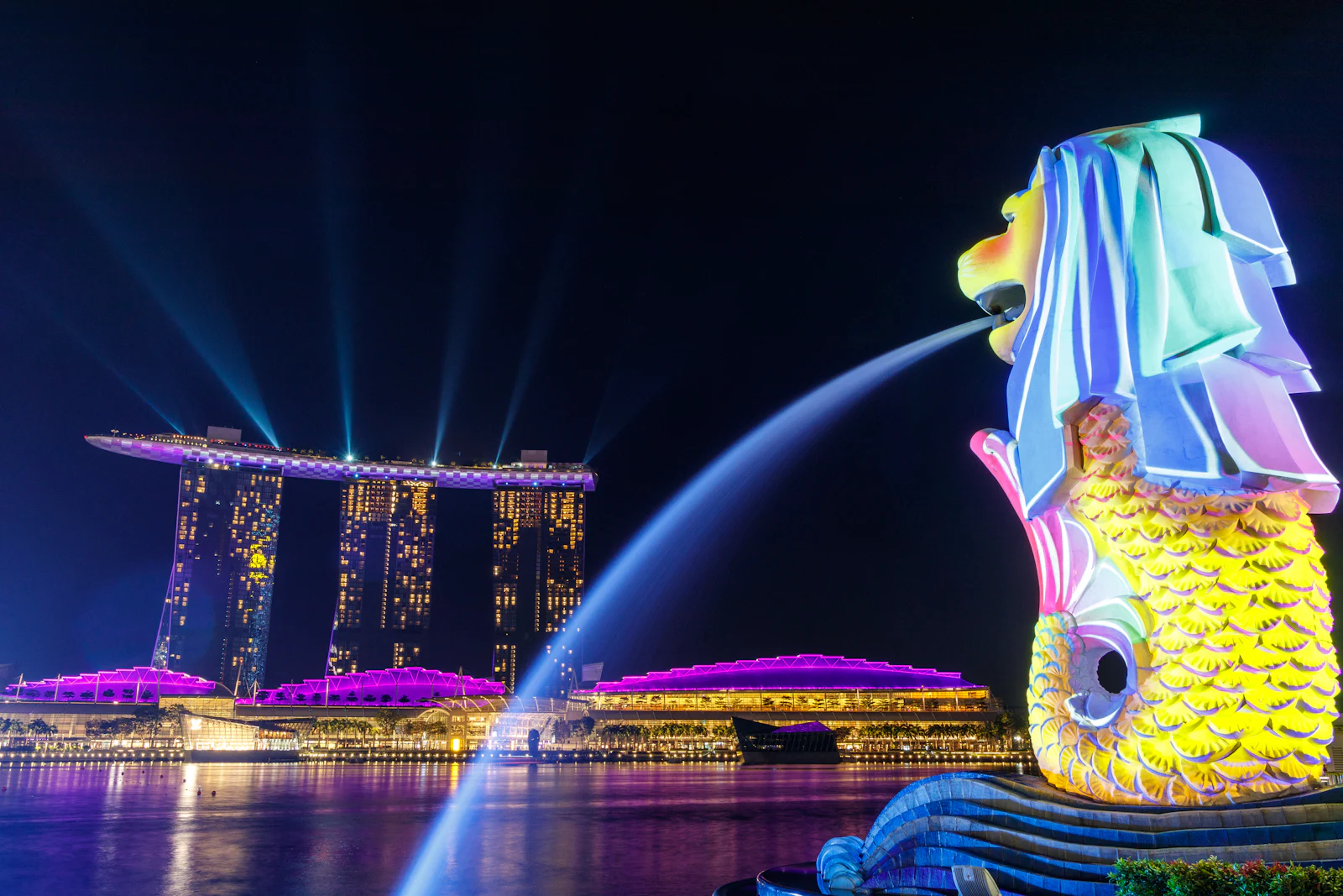 A waterfront skyline lit up at night with coloured lights reflecting on the bay