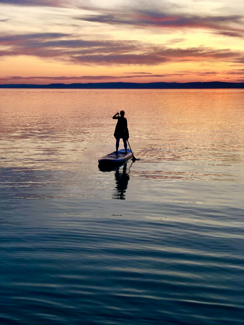 silhouette of person standing on paddle boat during golden hour