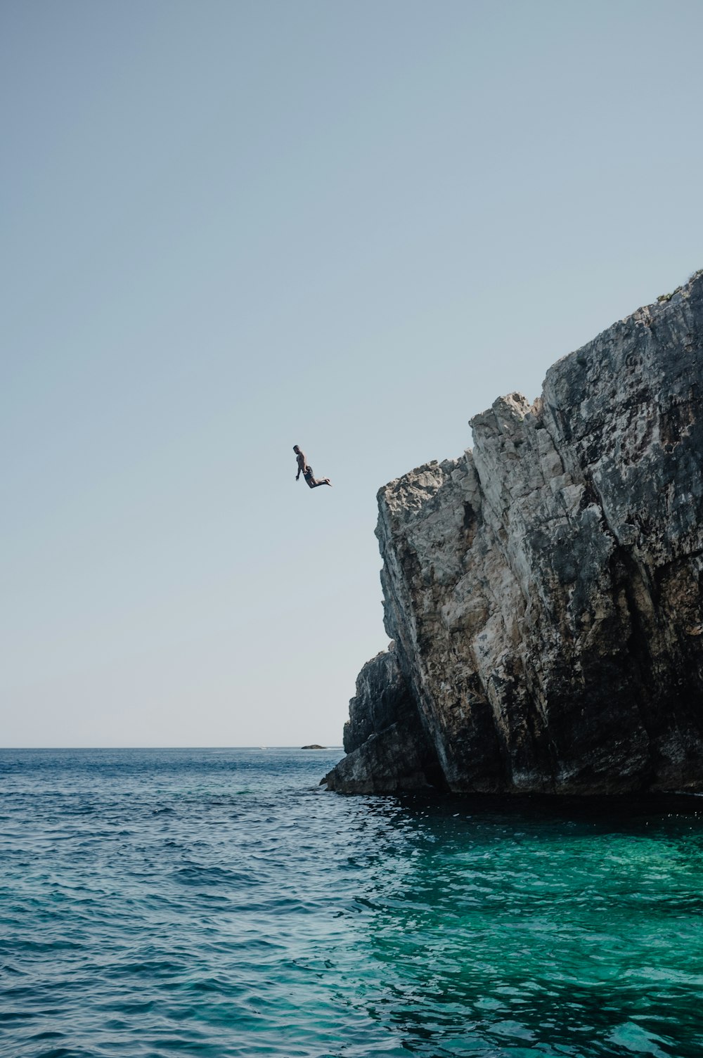 person jumping from rocky hill during daytime