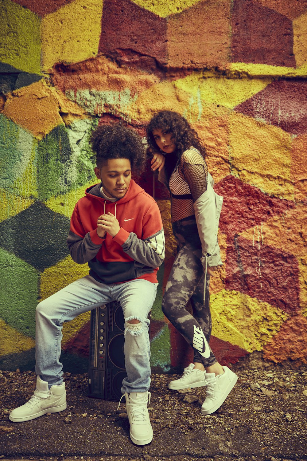 man and woman sitting and standing in front of red and yellow wall