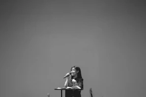 A professional woman delivering a keynote speech at a leadership forum with the bpw españa banner behind.