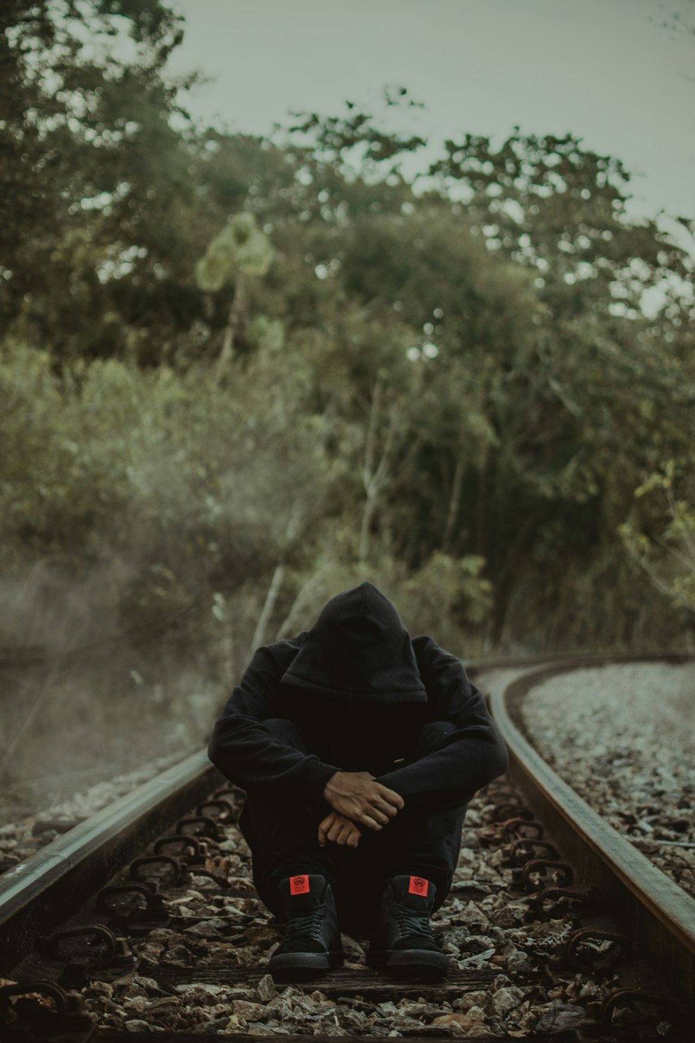photography of man sitting on ground between trail rail during daytime