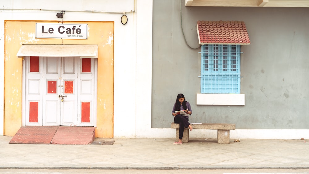 昼間、建物の横のコンクリートのベンチに座る女性