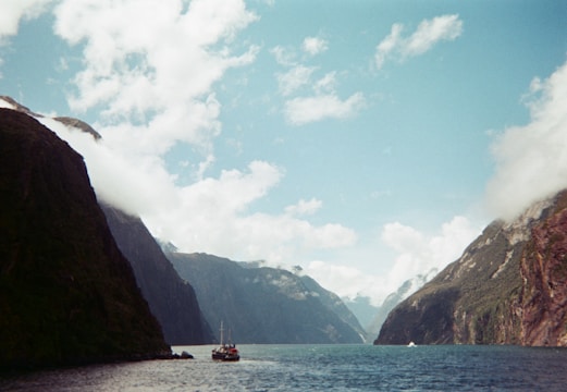 Image of a small boat cruising on calm fjord waters with forested hills in the background.