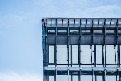 A modern glass building facade with metal supports against a clear blue sky, showcasing a grid-like pattern of windows.