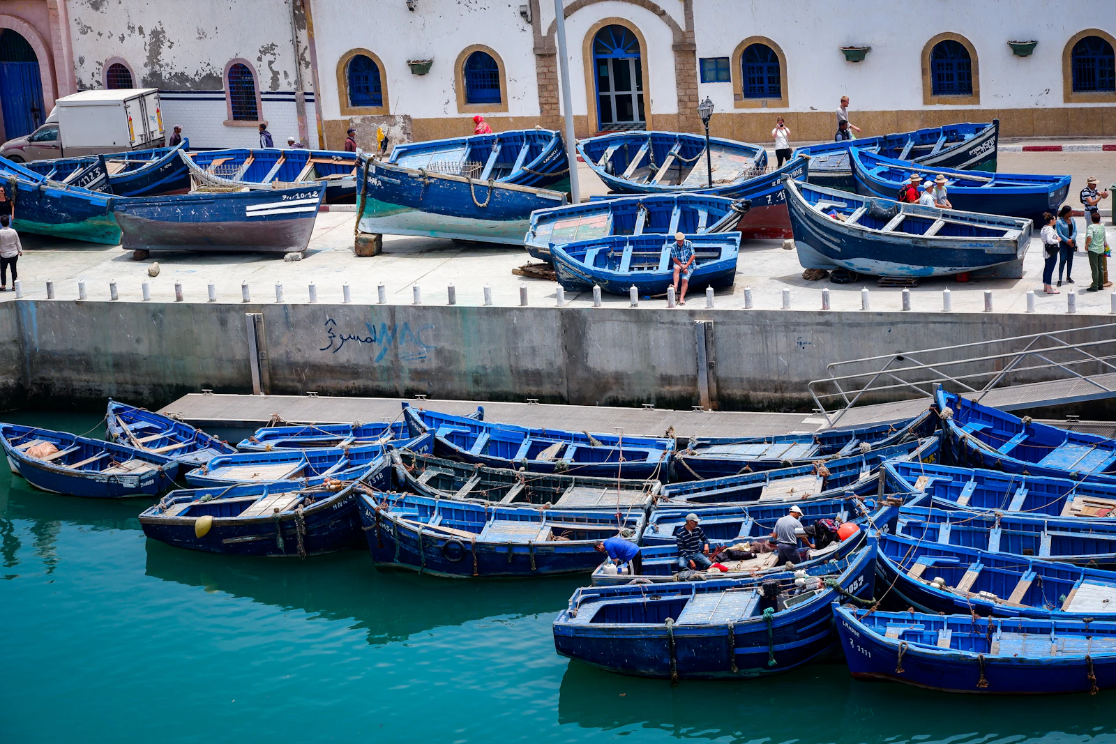 Blue wooden fishing boats clustered in the Essaouira harbor beside whitewashed port walls