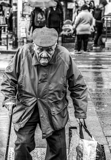 grayscale photo of man walking and holding handbag