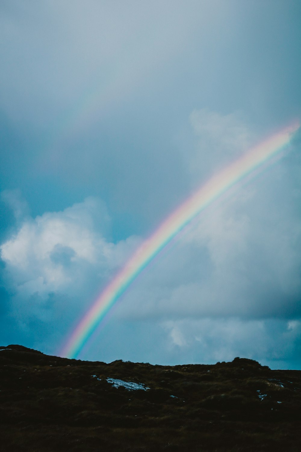 Ein Regenbogen erscheint am Himmel über einem Hügel