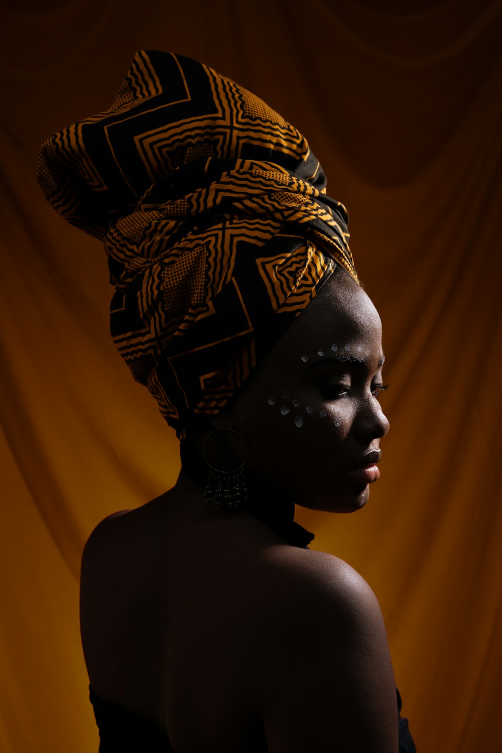 woman with black and orange turban standing and glancing her right side