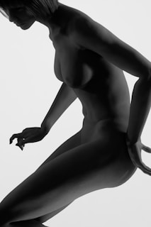 A grayscale image depicting a nude figure with short hair, captured from an angle that emphasizes the contours and musculature. The composition creates a classical yet modern aesthetic.