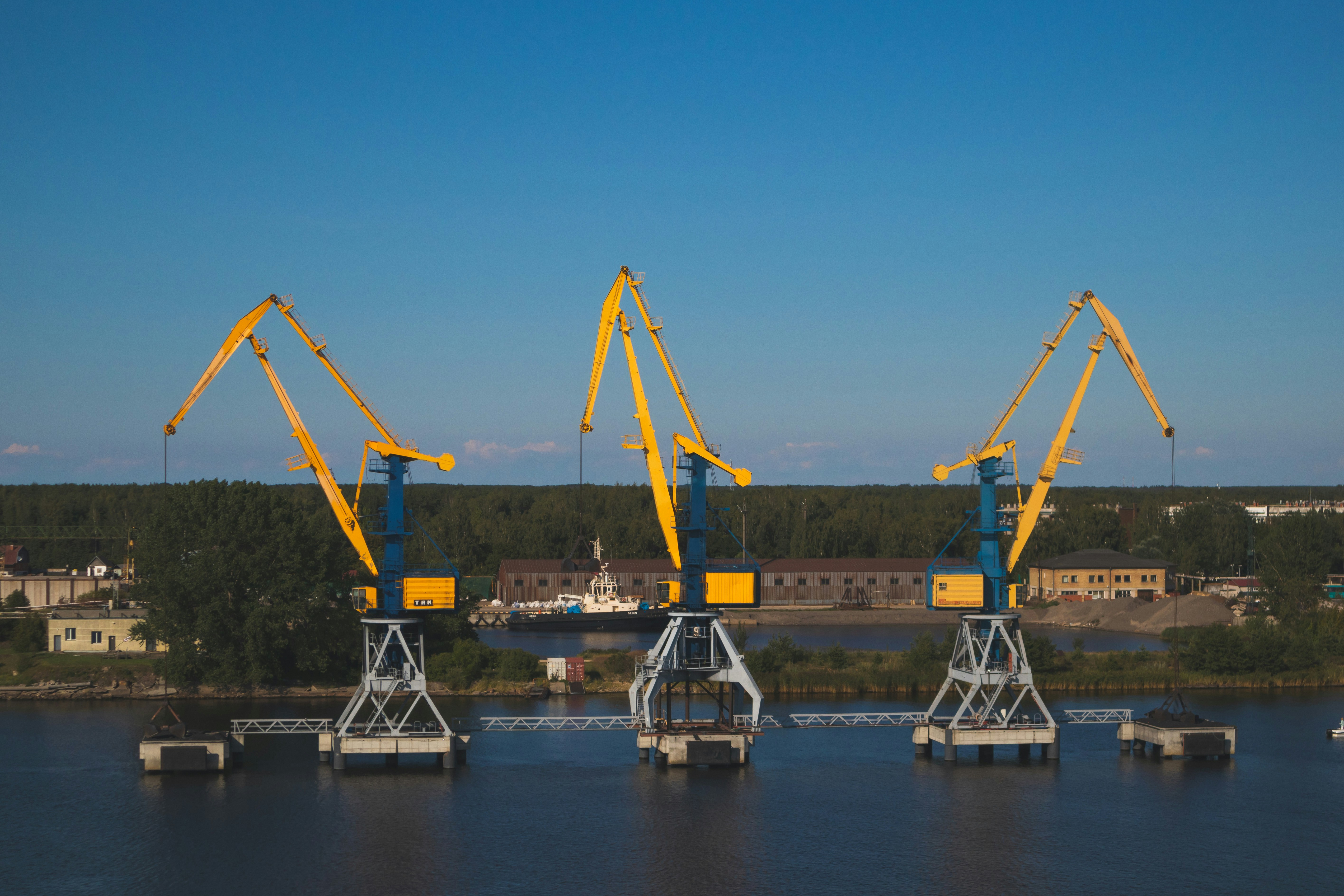 Three lined cranes near trees photo – Free Daugava river Image on Unsplash