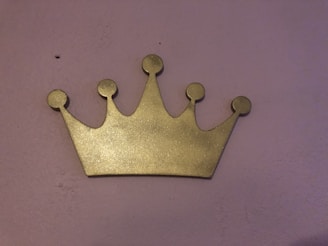 A delicate golden crown sparkling with tiny stars on a soft pink and lilac background.