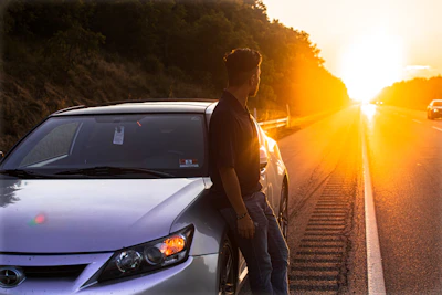 A roadside assistance vehicle helping a stranded car on a quiet highway at sunset.