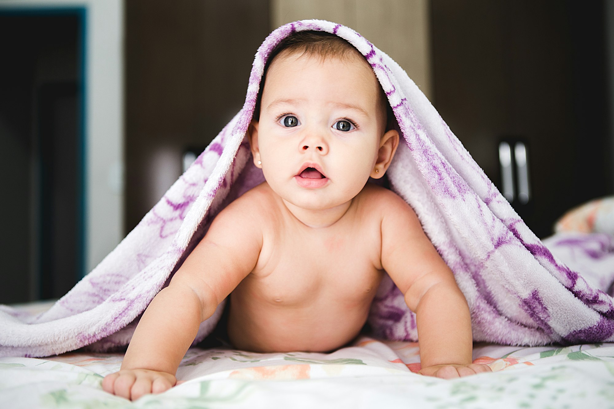 A baby crawling on a bed with a blanket over his or her body. 
