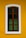 A wooden window with vertical bars is set against a vibrant yellow wall. The window frame is brown and the glass panes are dark, creating contrast with the surrounding white border.