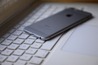 A smartphone is placed face down on the keyboard of a laptop, creating a modern tech workspace setting. The focus is on the smartphone, and the keyboard keys are visible around it.