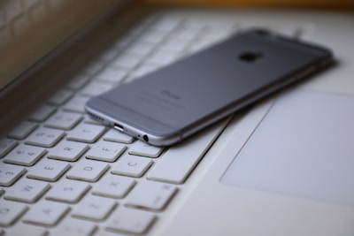 A smartphone is placed face down on the keyboard of a laptop, creating a modern tech workspace setting. The focus is on the smartphone, and the keyboard keys are visible around it.