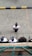 A group of security personnel wearing uniforms and caps standing on a tiled pavement, viewed from above. The tiles are organized in a geometric pattern, and there's a black and yellow curb visible at the top of the image.