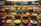 A display case filled with a variety of decorated cakes showcasing intricate designs and vibrant colors. Each cake features unique patterns, toppings, and decorations such as chocolate shavings, fruit slices, and colorful icing. The cakes are arranged neatly in rows across multiple shelves.