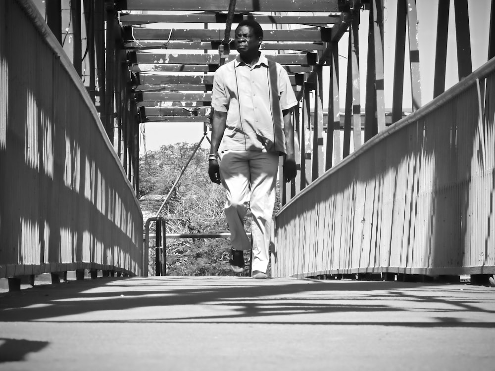 grayscale photo of a man walking on a bridge