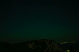 A retro sci-fi UFO hovering silently above a dark mountain ridge under a starry sky.