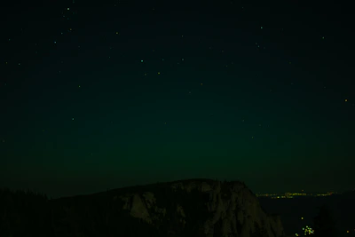 A retro sci-fi UFO hovering silently above a dark mountain ridge under a starry sky.