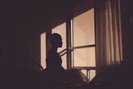 A woman journaling by a window with morning light filtering through sheer curtains.