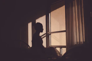A woman sitting quietly by a window, bathed in warm morning light.