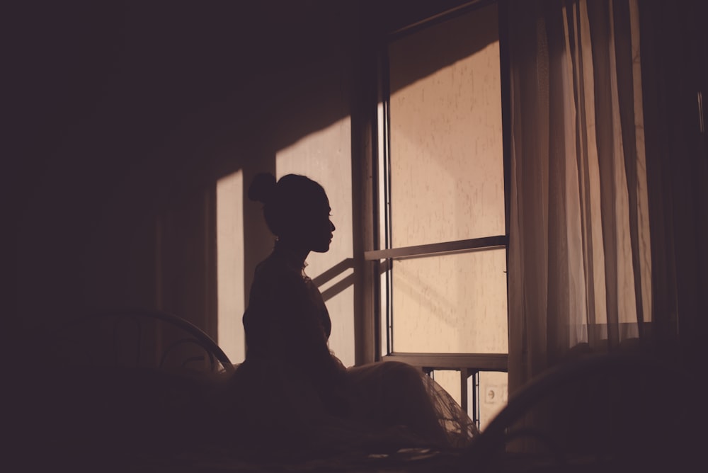 a woman sitting on a bed in front of a window