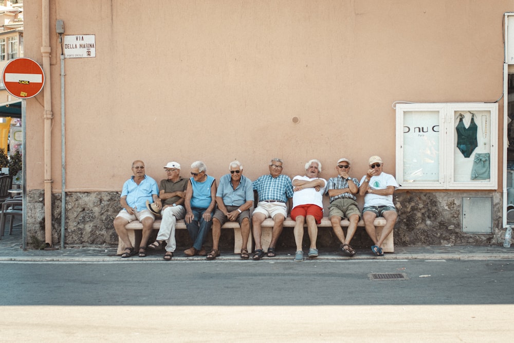 낮에 오렌지 벽 근처 벤치에 앉아 있는 여덟 명의 남자