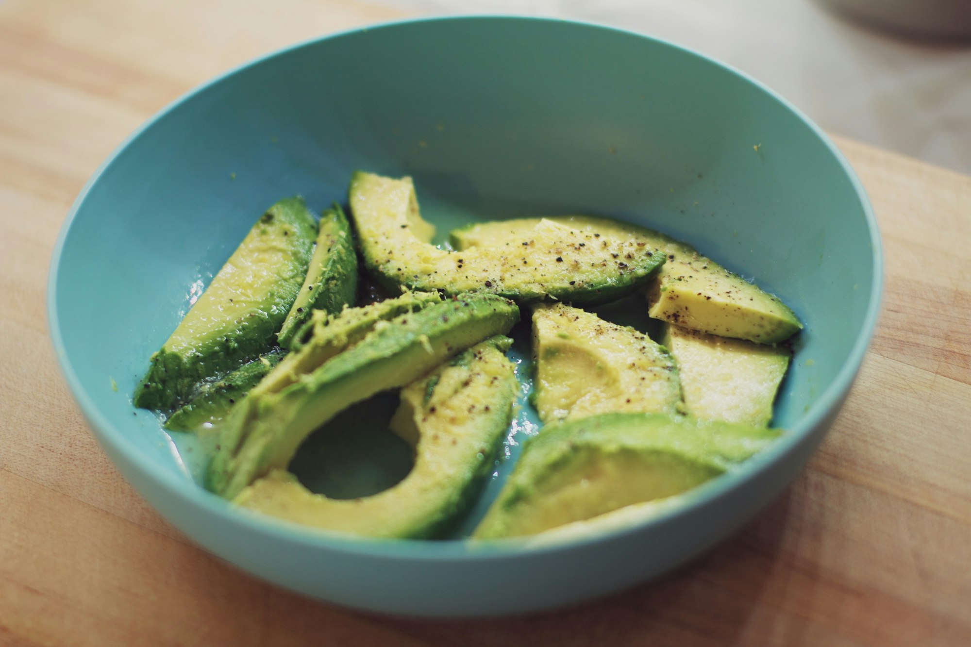 Sliced avocados in a teal bowl on a cutting board.