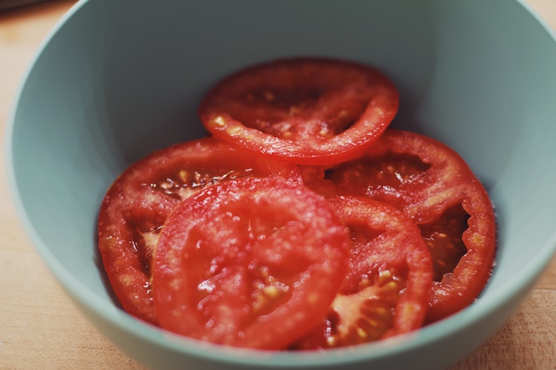 Sliced tomatoes in a teal bowl on a cutting board. from unsplash}