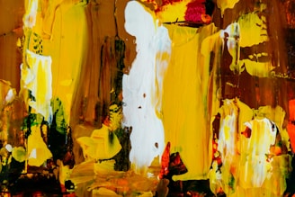 An abstract painting featuring bold strokes and splashes of color. The piece consists predominantly of vibrant yellows, earthy browns, and bright whites with some touches of red and green. The textures are thick and expressive, creating a dynamic and energetic composition.