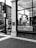 A black and white photograph depicts the storefront of a cafe called 'The Caffeinery' with a large logo featuring a coffee pot. The window is filled with words related to coffee and bakery items. It's located in a brick building, and nearby is a street sign and a lamppost.